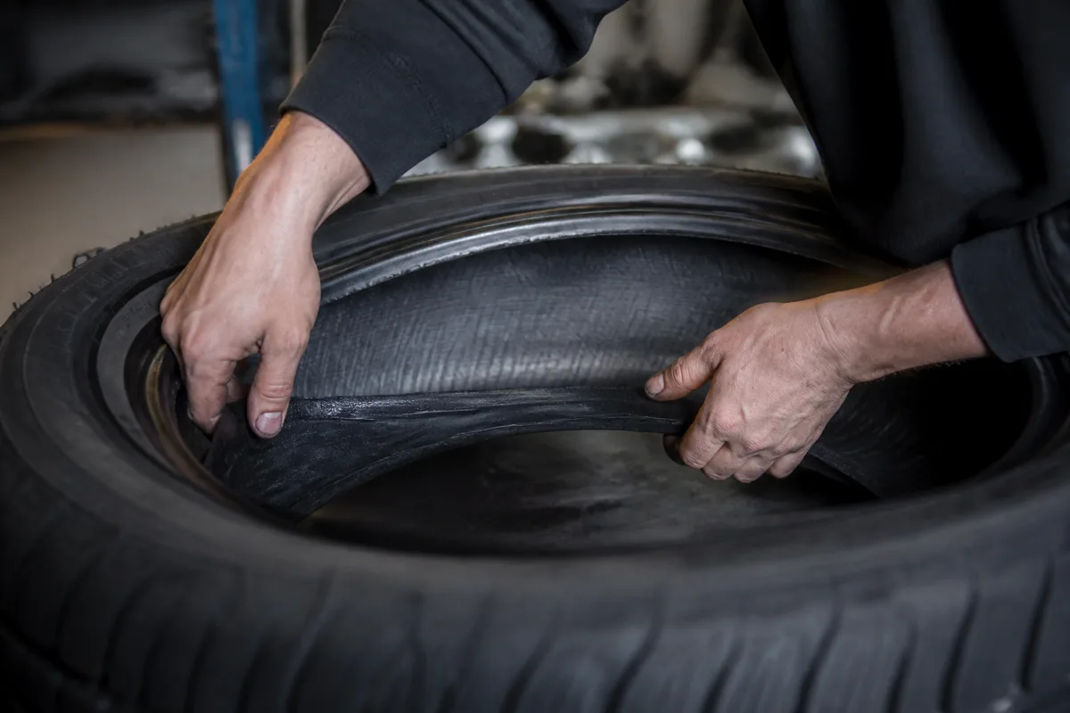 Inspection à la main de l&rsquo;intérieur d&rsquo;une enveloppe de pneu posée à plat dans un atelier